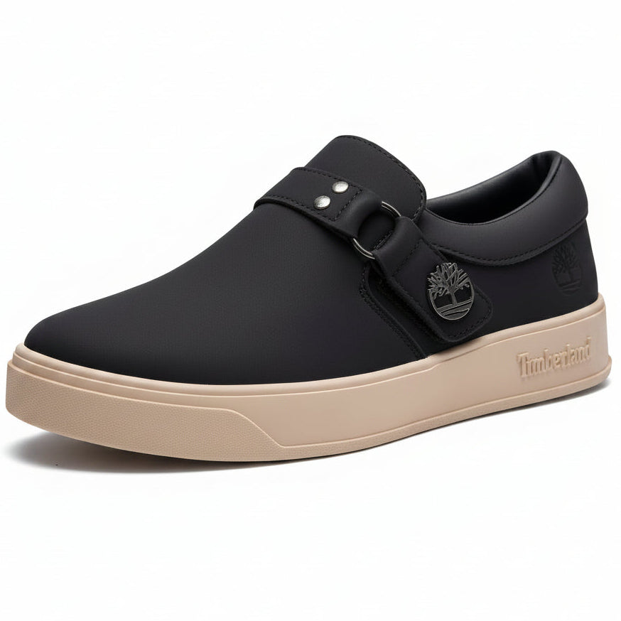Black sneaker with beige sole held by a hand against a green leafy background