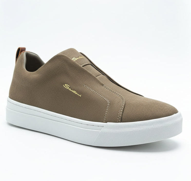 Brown slip-on sneaker with white sole held by a hand in front of green plants.
