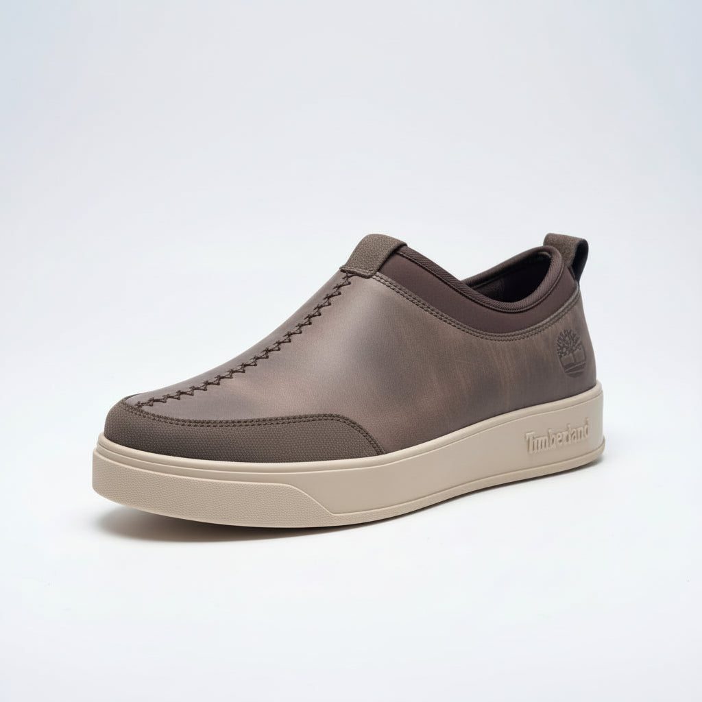 Brown Timberland shoe held in front of green foliage