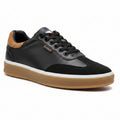 Black sneaker with brown accents held by a hand on a blurred background