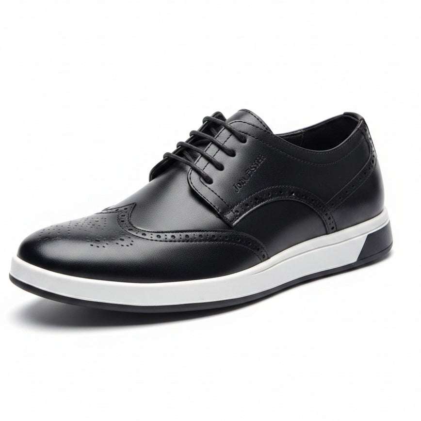 Black leather shoe with white sole held by a hand, with another shoe and blue box in the background on a concrete floor.