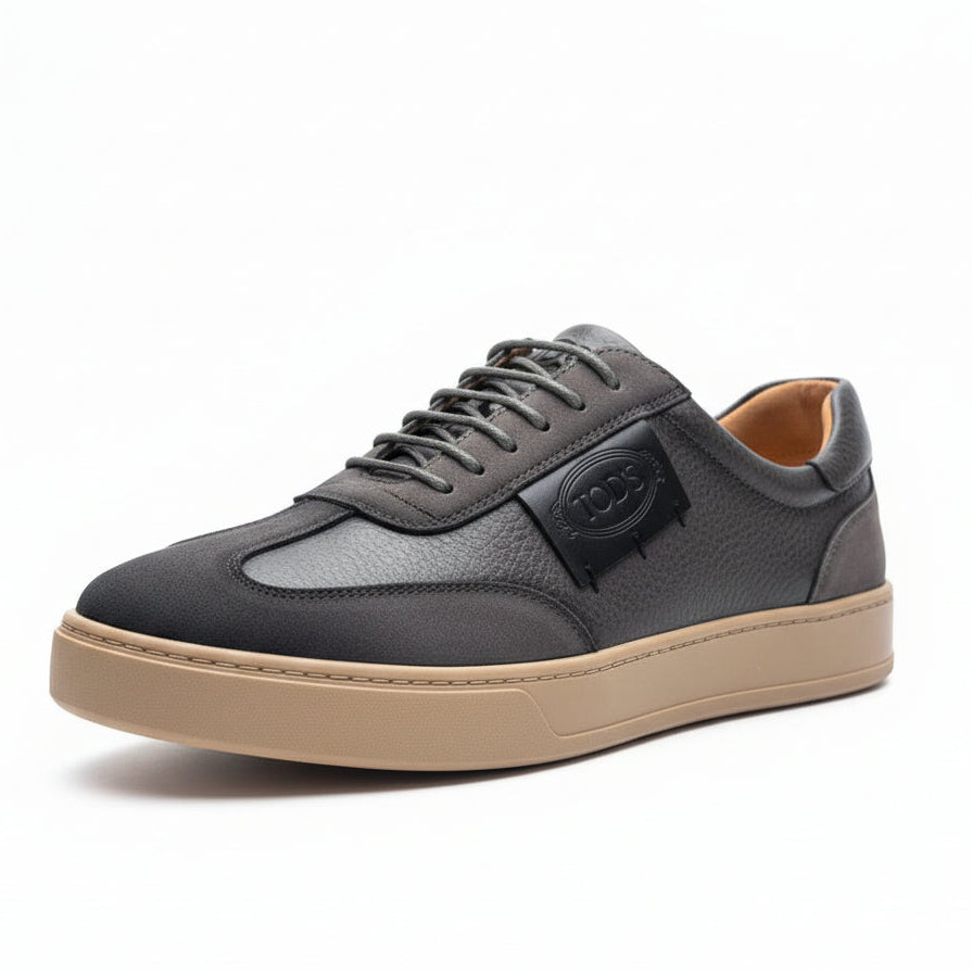Gray sneaker with beige sole held by a hand against a green leafy background