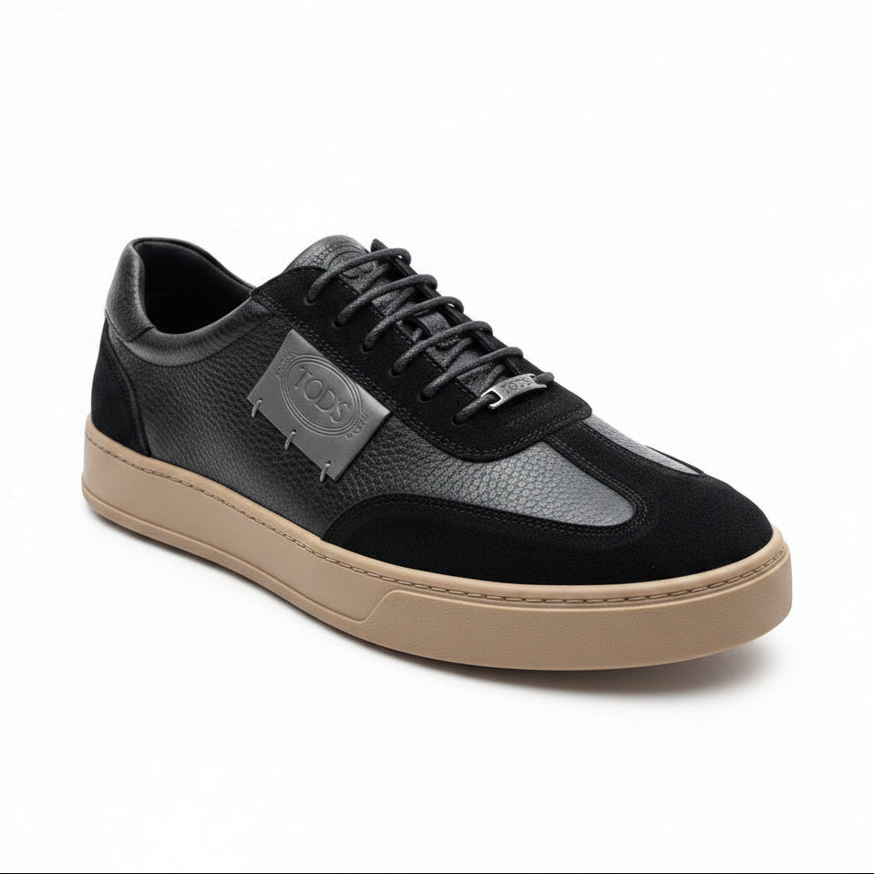 Black and beige sneaker held by a hand with a plant in the background