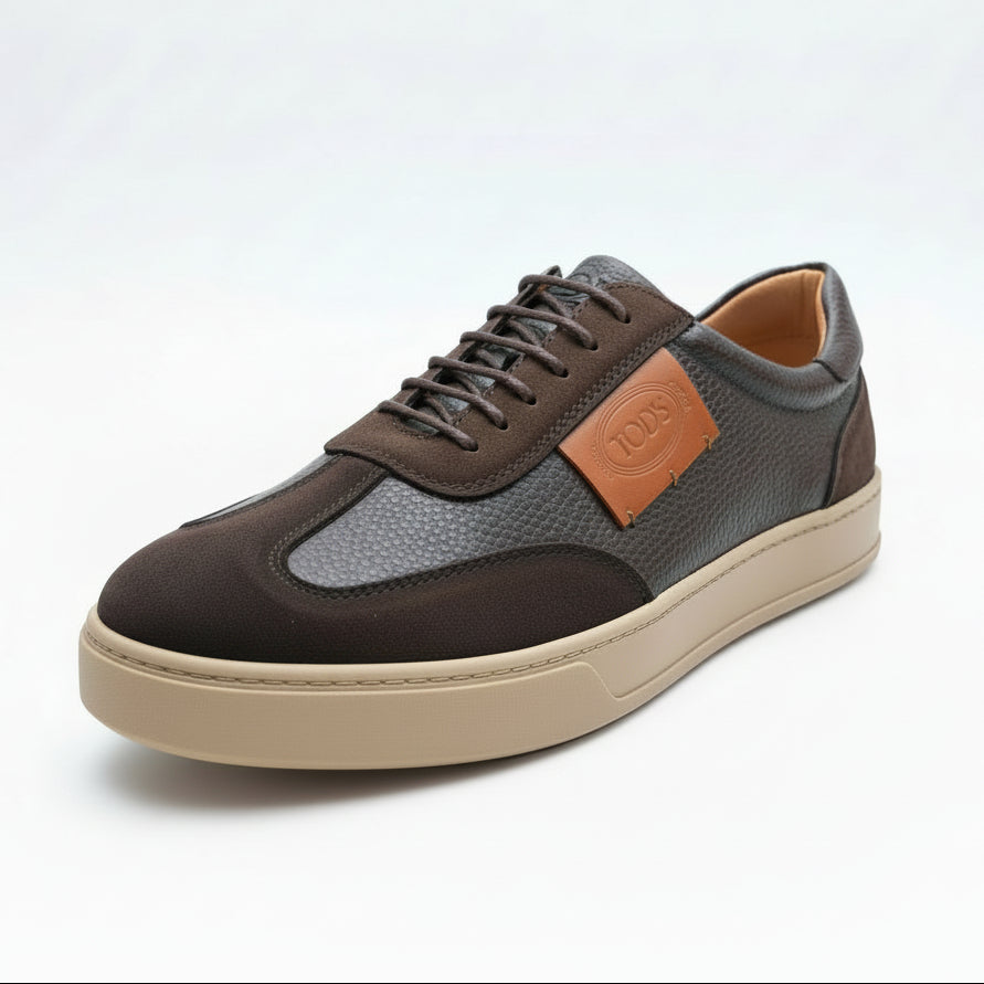 Brown and gray sneaker with orange patch held by a hand against a green plant background